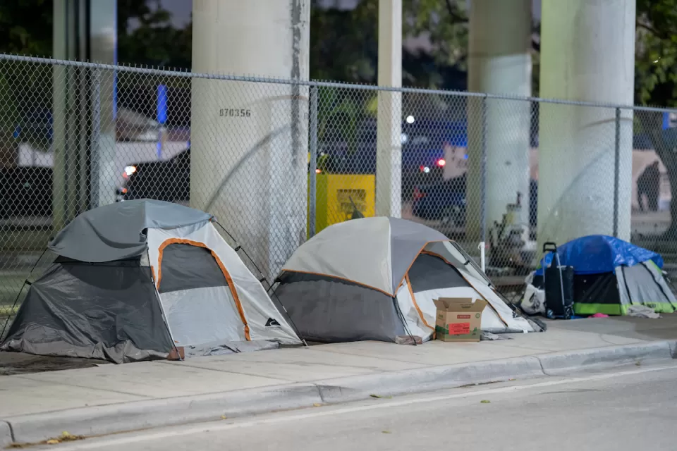 Three small tents set up on sidewalk under overpass in Miami, Florida.